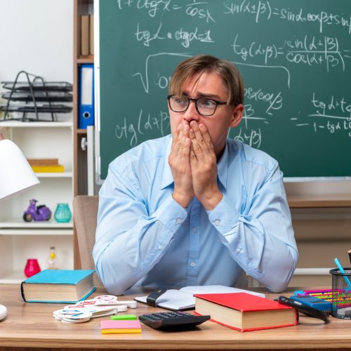 Professor sentado na sala de aula pensando em como lidar com o mau comportamento dos alunos